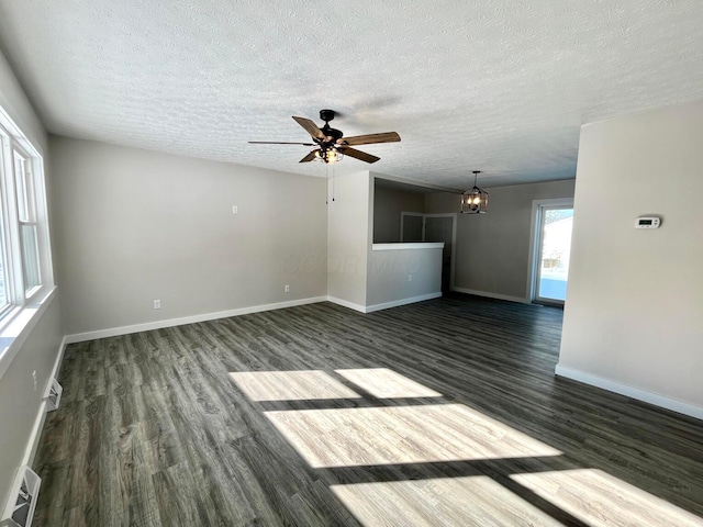 empty room featuring a textured ceiling, ceiling fan with notable chandelier, a wealth of natural light, and dark wood-type flooring