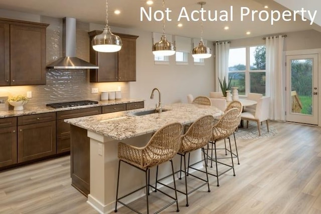 kitchen featuring wall chimney exhaust hood, a breakfast bar area, stainless steel gas cooktop, and a center island with sink