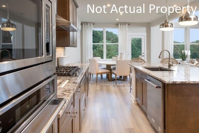 kitchen with hanging light fixtures, appliances with stainless steel finishes, sink, and a kitchen island with sink