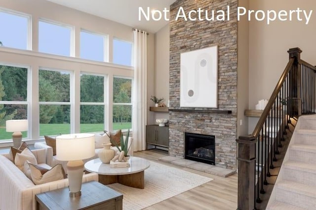 living room with a towering ceiling, a stone fireplace, and light hardwood / wood-style floors