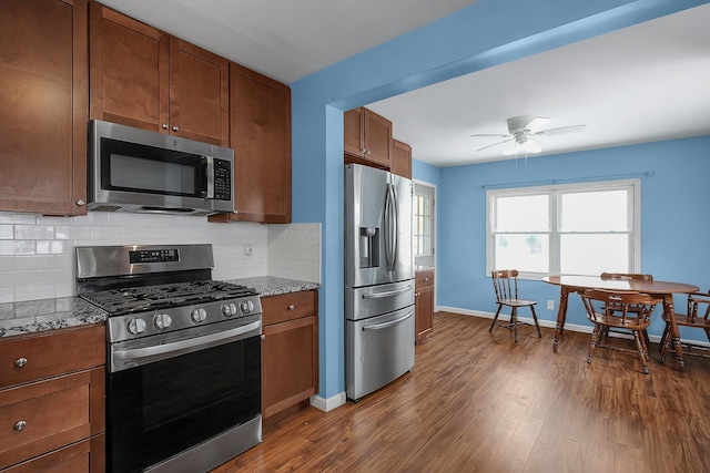 kitchen featuring appliances with stainless steel finishes, tasteful backsplash, ceiling fan, dark wood-type flooring, and stone countertops