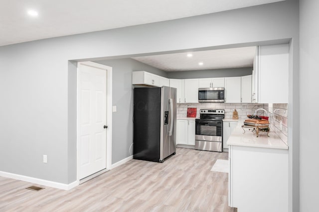 kitchen featuring tasteful backsplash, stainless steel appliances, sink, light hardwood / wood-style flooring, and white cabinets