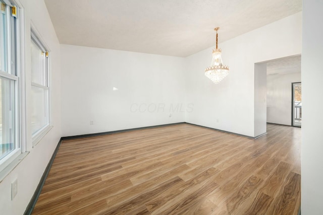 empty room with a notable chandelier and wood-type flooring