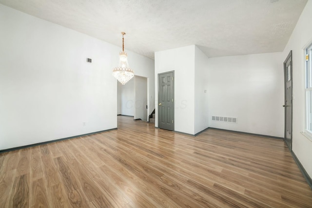 empty room with hardwood / wood-style flooring, a textured ceiling, and a chandelier