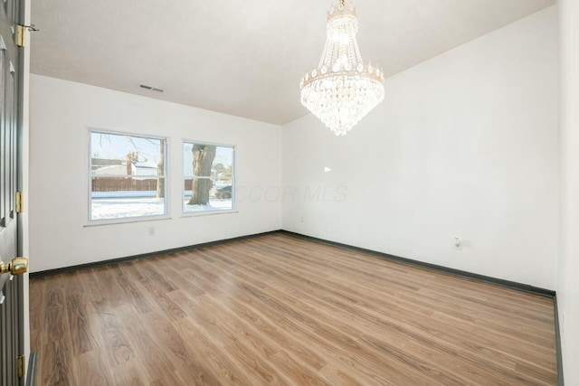 spare room featuring wood-type flooring and an inviting chandelier