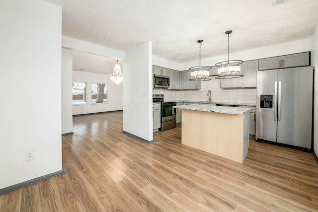 kitchen with light stone countertops, appliances with stainless steel finishes, decorative backsplash, gray cabinetry, and a center island