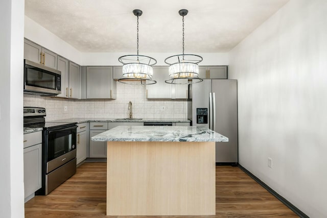 kitchen featuring a center island, an inviting chandelier, sink, light stone countertops, and appliances with stainless steel finishes