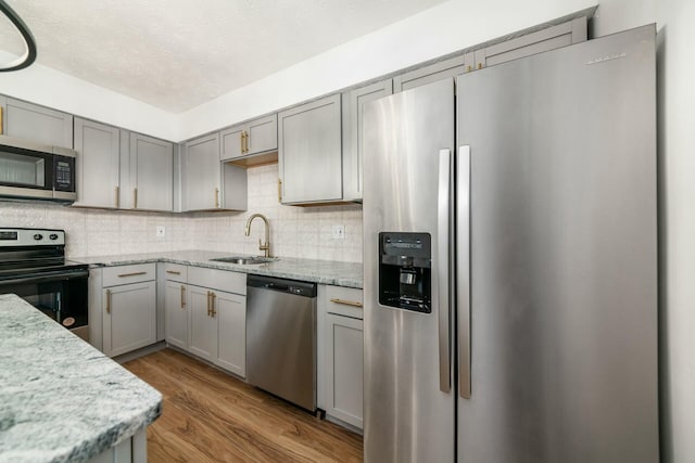 kitchen featuring sink, decorative backsplash, light stone countertops, light wood-type flooring, and appliances with stainless steel finishes