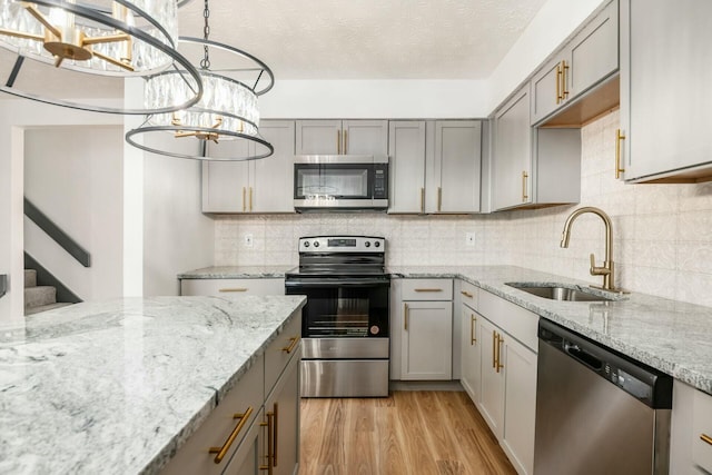 kitchen with appliances with stainless steel finishes, gray cabinetry, sink, pendant lighting, and light hardwood / wood-style flooring