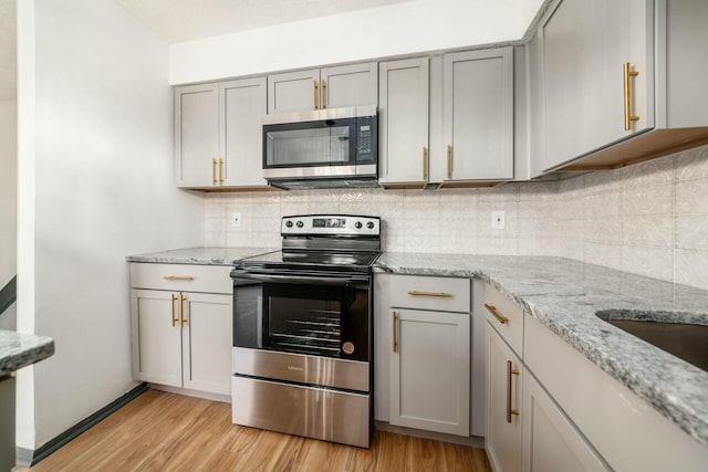 kitchen featuring gray cabinetry, light hardwood / wood-style floors, light stone countertops, and appliances with stainless steel finishes