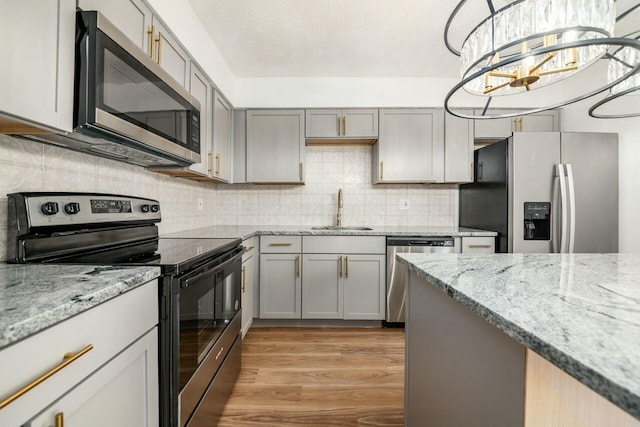 kitchen with gray cabinetry, sink, light stone countertops, light hardwood / wood-style floors, and stainless steel appliances