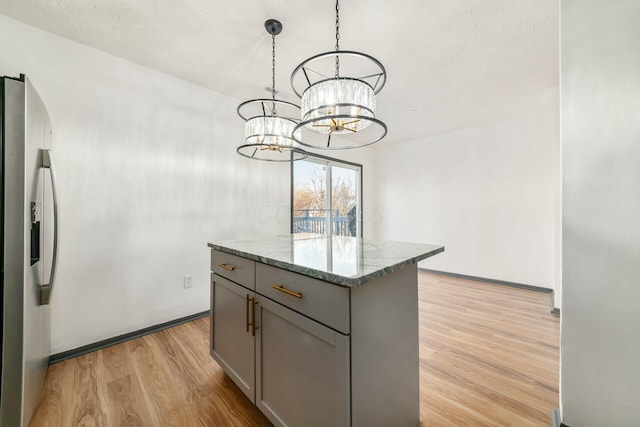 kitchen featuring light stone countertops, stainless steel fridge with ice dispenser, decorative light fixtures, gray cabinets, and a kitchen island