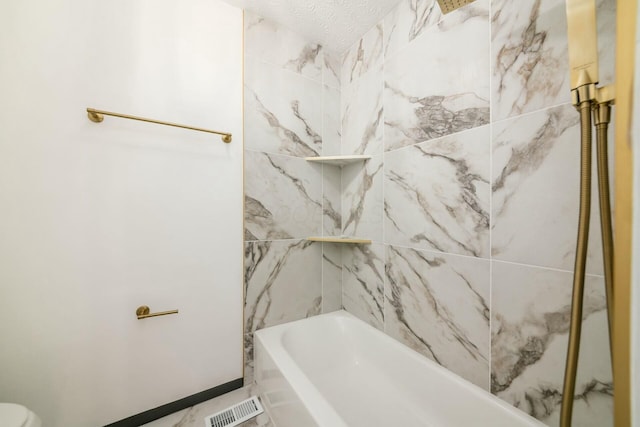 bathroom with a textured ceiling and tiled shower / bath