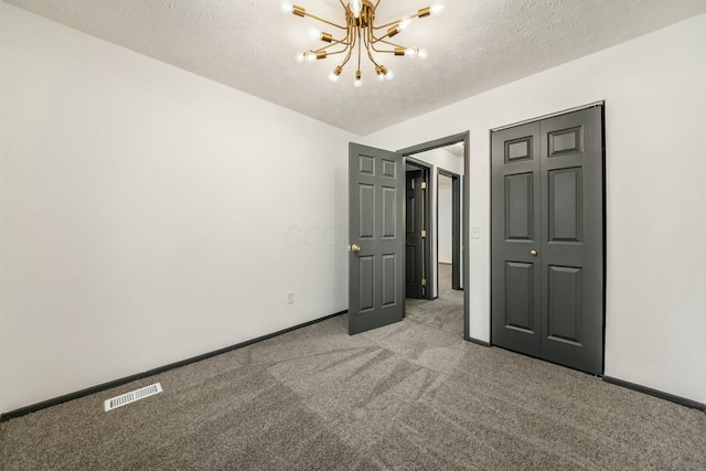 unfurnished bedroom with a closet, light colored carpet, a textured ceiling, and an inviting chandelier