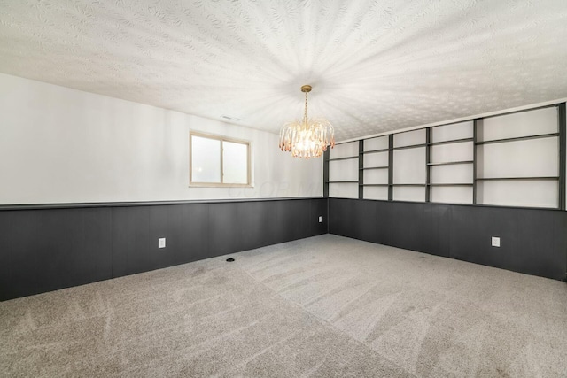 empty room with a chandelier, carpet, a textured ceiling, and wooden walls