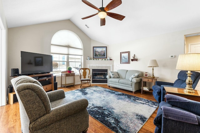 living room featuring ceiling fan, a tiled fireplace, high vaulted ceiling, and light wood-type flooring