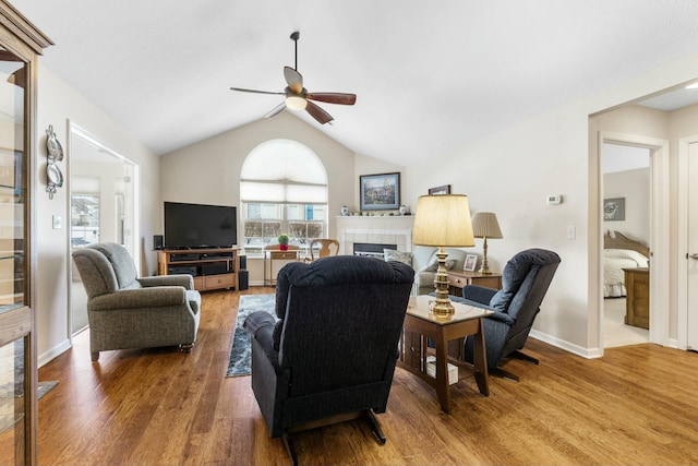 living room with a tiled fireplace, wood-type flooring, vaulted ceiling, and ceiling fan