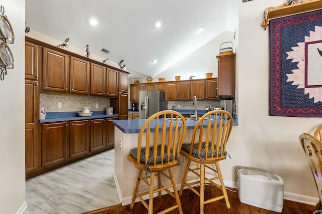 kitchen with vaulted ceiling, backsplash, light hardwood / wood-style floors, and stainless steel fridge with ice dispenser