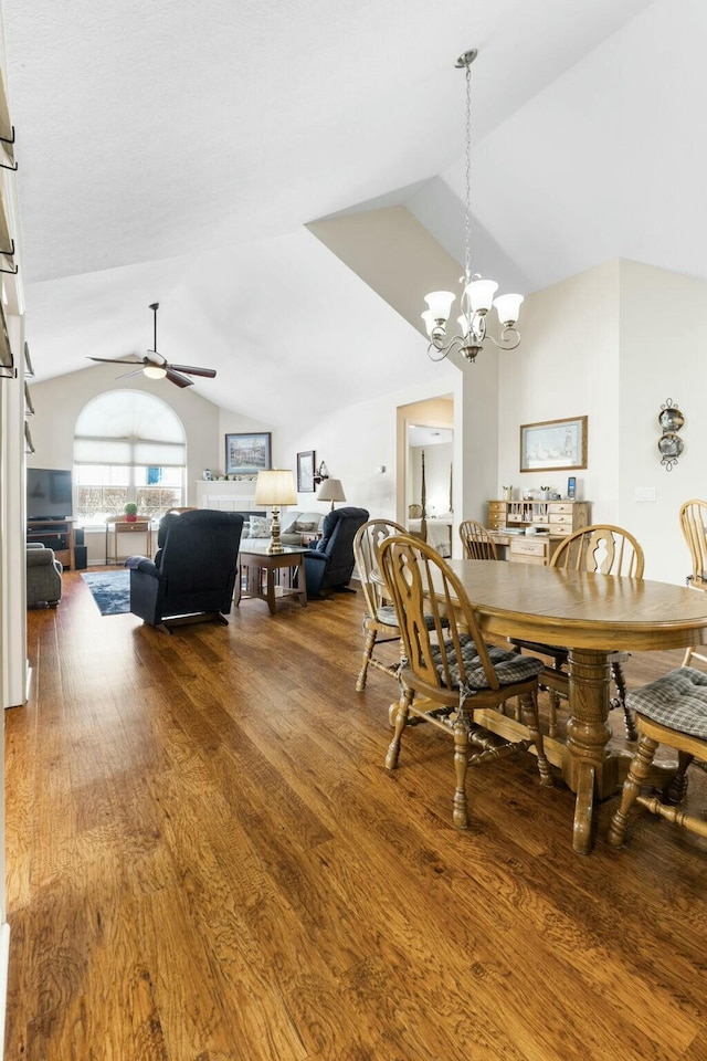 dining area with ceiling fan with notable chandelier, wood-type flooring, and vaulted ceiling