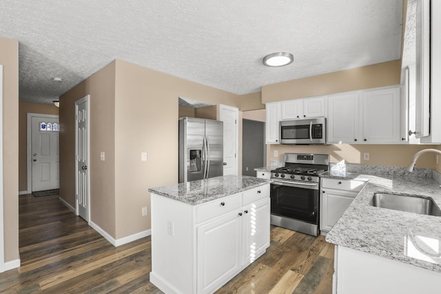 kitchen with stainless steel appliances, light stone countertops, sink, and white cabinets