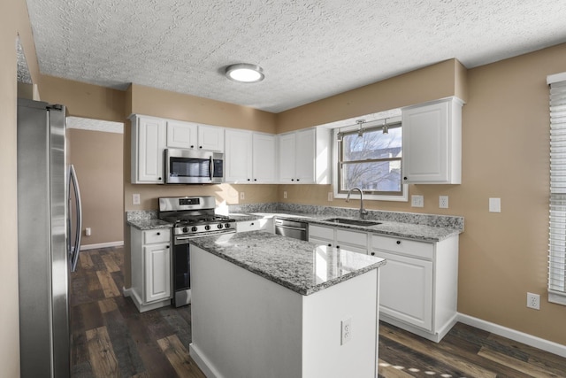 kitchen featuring sink, light stone counters, a center island, stainless steel appliances, and white cabinets