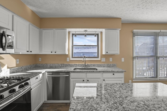 kitchen featuring sink, a textured ceiling, stainless steel appliances, light stone countertops, and white cabinets