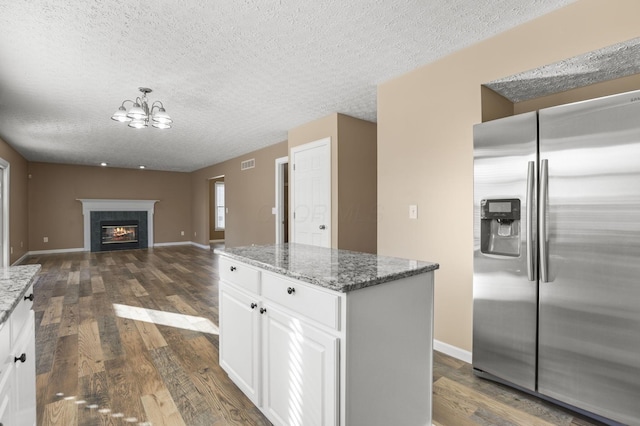 kitchen featuring dark stone countertops, stainless steel fridge, a tile fireplace, and white cabinets