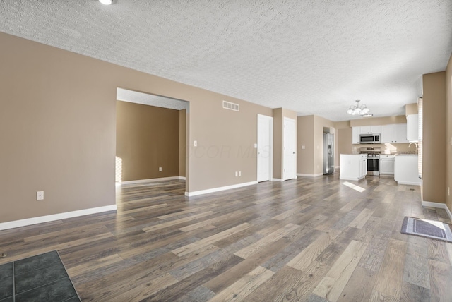 unfurnished living room featuring dark hardwood / wood-style floors, a chandelier, sink, and a textured ceiling