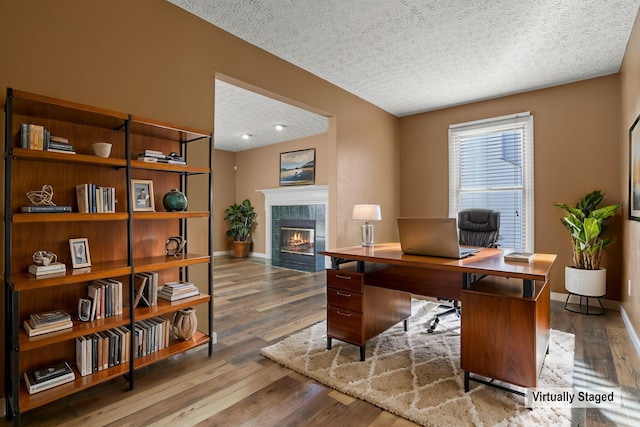 home office featuring wood-type flooring, a fireplace, and a textured ceiling