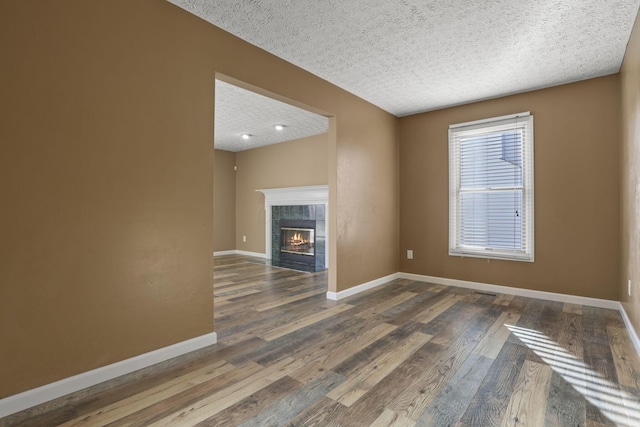 unfurnished living room with a tiled fireplace, dark wood-type flooring, and a textured ceiling