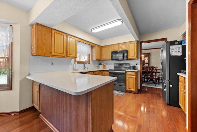 kitchen featuring kitchen peninsula, appliances with stainless steel finishes, backsplash, sink, and wood-type flooring