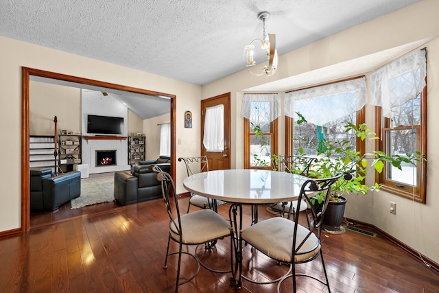 dining area featuring a textured ceiling, dark hardwood / wood-style floors, a fireplace, and an inviting chandelier