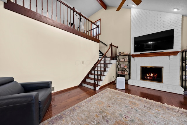 living room with vaulted ceiling with beams, ceiling fan, dark wood-type flooring, and a brick fireplace