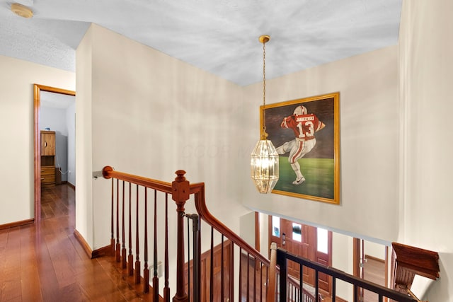 staircase with hardwood / wood-style flooring, a textured ceiling, and an inviting chandelier