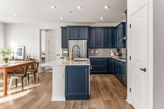 kitchen featuring stainless steel refrigerator, light wood-type flooring, a kitchen island with sink, and blue cabinets