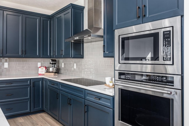 kitchen with appliances with stainless steel finishes, blue cabinetry, wall chimney range hood, and tasteful backsplash