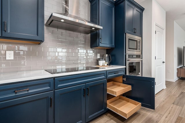 kitchen featuring wall chimney exhaust hood, stainless steel appliances, tasteful backsplash, light wood-type flooring, and blue cabinets