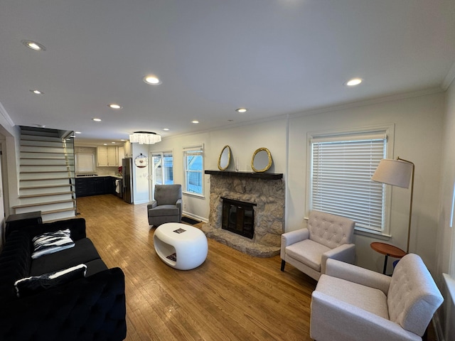 living room featuring an inviting chandelier, hardwood / wood-style flooring, a stone fireplace, and ornamental molding