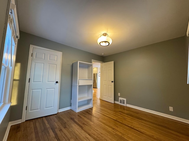 unfurnished bedroom with stainless steel fridge and hardwood / wood-style floors