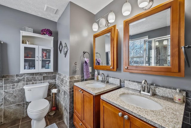 bathroom featuring tile patterned floors, a textured ceiling, toilet, vanity, and tile walls