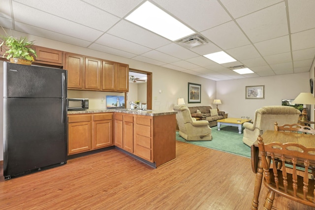 kitchen featuring kitchen peninsula, light hardwood / wood-style floors, a drop ceiling, and black appliances