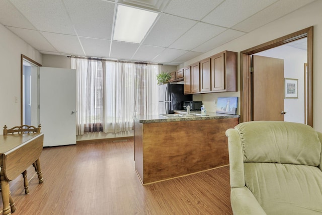 kitchen with a paneled ceiling, light hardwood / wood-style flooring, black fridge, and sink