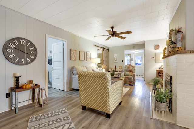 living room with hardwood / wood-style flooring, a fireplace, a barn door, and ceiling fan