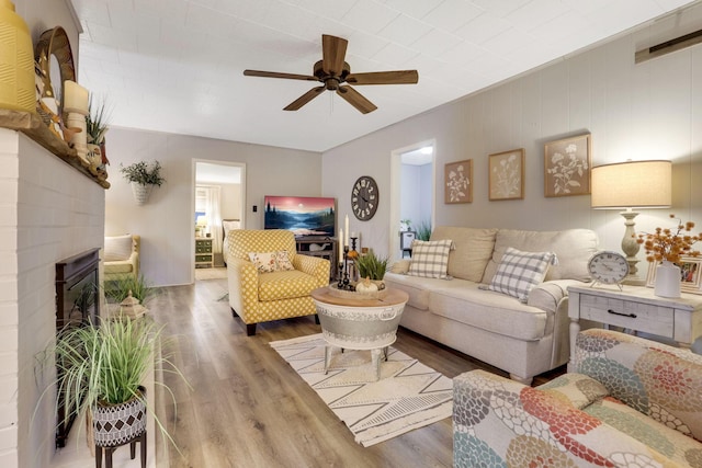 living room with ceiling fan, wood-type flooring, and a brick fireplace