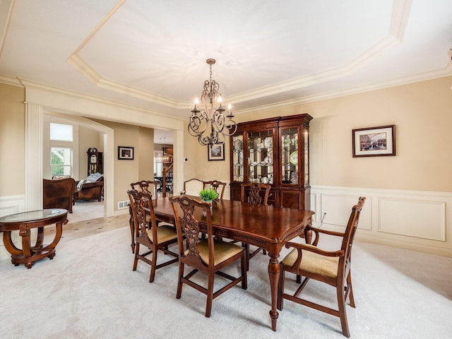 carpeted dining area featuring a tray ceiling, ornamental molding, and a chandelier