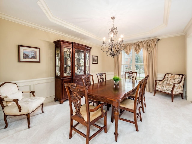 dining space featuring a raised ceiling, ornamental molding, light carpet, and a chandelier