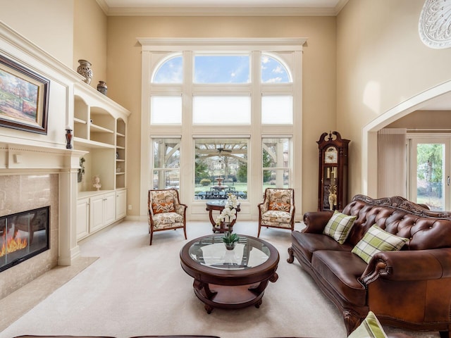 living room featuring a towering ceiling, ornamental molding, a tile fireplace, and light carpet