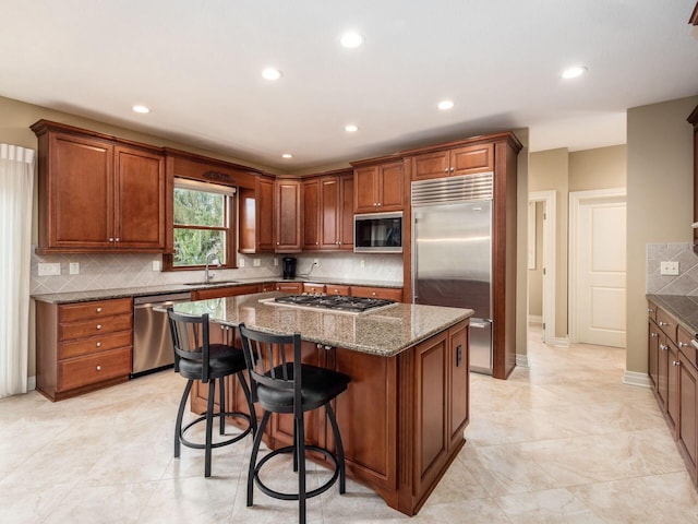 kitchen featuring sink, dark stone countertops, backsplash, built in appliances, and a kitchen island