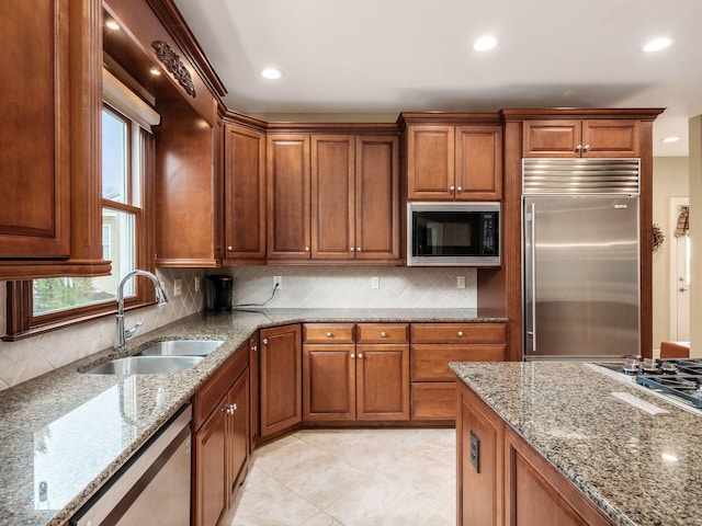 kitchen with light stone counters, built in appliances, sink, and decorative backsplash