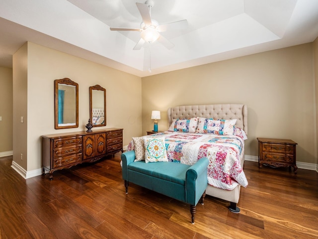 bedroom with dark wood-type flooring, a raised ceiling, and ceiling fan